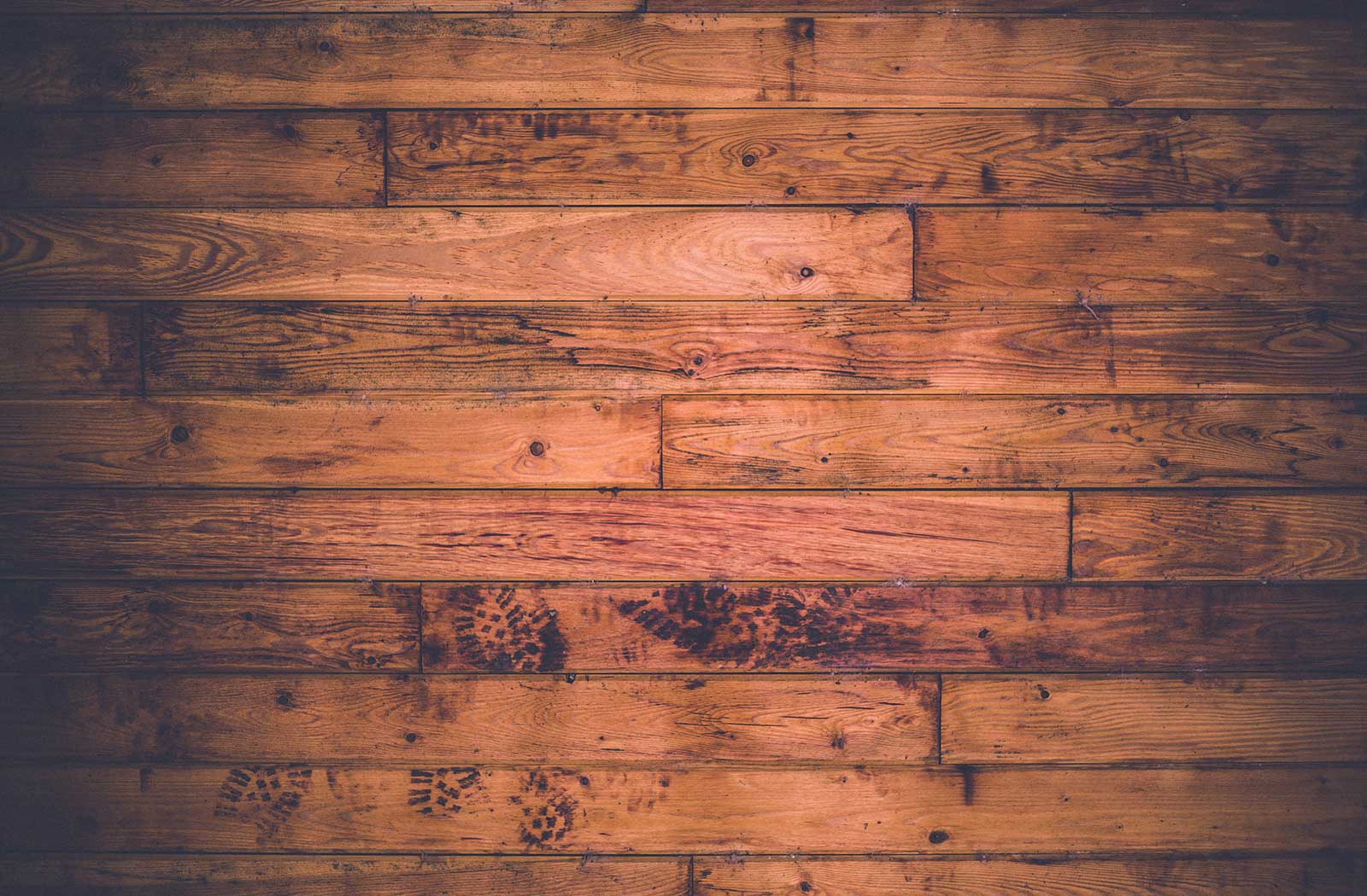Close-up of weathered wooden plank flooring with visible boot print marks, warm brown tones